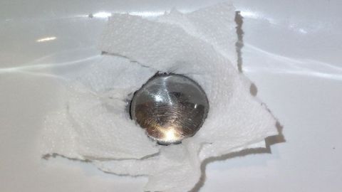 Undichten Stöpsel im Waschbecken mit Küchenpapier abdichten. Ein dichter Stöpsel liegt in einem Spülbecken, umgeben von feuchtem Küchenpapier, während Wasser austritt.
