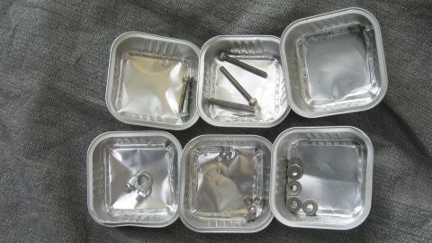 Kleine Schalen von Katzenfutter organisieren Schrauben und Kleinteile auf einem dunklen Untergrund im Hobbyraum.