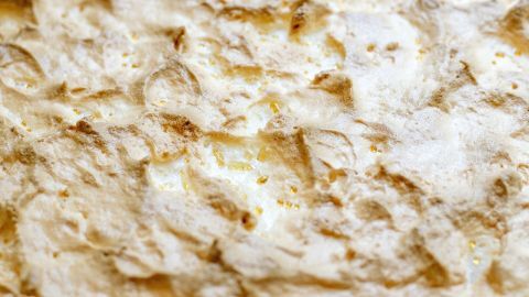 Ein großer, krümeliger Goldtränenkuchen liegt auf einer Fläche und präsentiert eine goldbraune Oberfläche mit unregelmäßiger Textur.