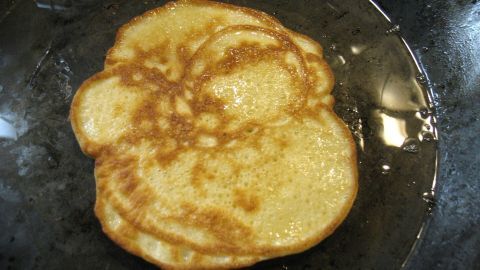 Ein goldbrauner Eierkuchen brät in einer Pfanne, umgeben von einem leichten Ölfilm, und zeigt eine schöne, luftige Textur.