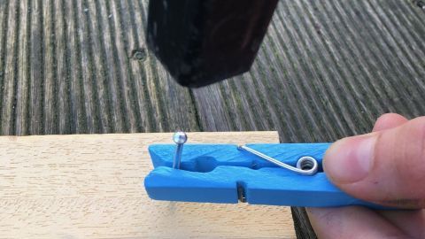 Ein blauer Nagelhalter wird benutzt, um einen Nagel präzise in ein Holzbrett zu schlagen, ohne blaue Finger zu bekommen.