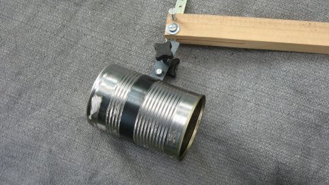 Ein metallischer Eimer hängt an einem Holzarm und wird zur Reinigung der Regenrinne verwendet. Die Umgebung ist grau und neutral.