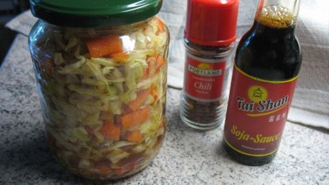 Ein Einmachglas mit Kimchi aus Spitzkohl steht neben Gewürz und Sojasauce auf einer Tischoberfläche.
