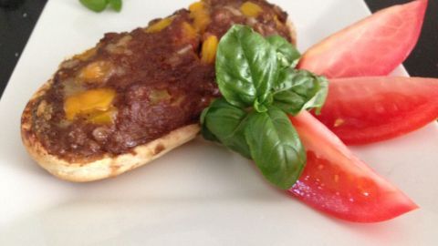 Ein Hackfleischbrötchen liegt auf einem weißen Teller, garniert mit frischem Basilikum und Tomatenscheiben.