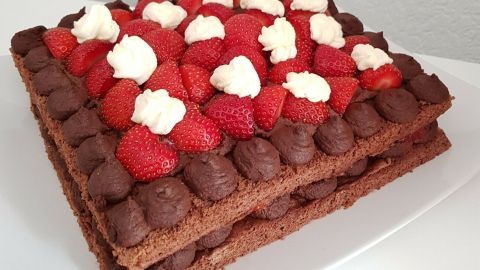 Eine saftige Schokoladen-Biskuit-Torte, dekoriert mit Erdbeeren und Sahne, steht auf einem weißen Teller in einer minimalistischen Umgebung.
