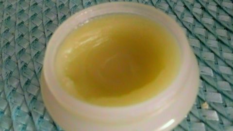 Eine kleine, runde Dose mit gelber Mückenstich-Salbe steht auf einer geflochtenen, grünen Unterlage.