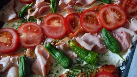 Eine Coca con verduras, belegt mit frischen Tomatenscheiben, Schinken und grünen Paprikaschoten, liegt auf einem Blech.