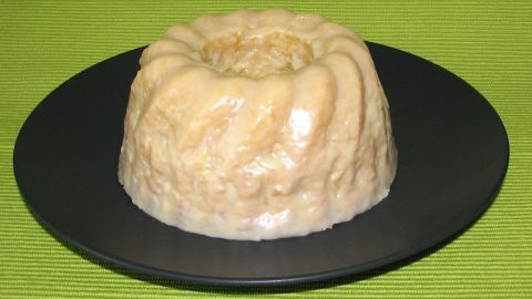 Ein Pina-Colada-Kuchen steht auf einem schwarzen Teller und glänzt appetitlich vor einem grünen Untergrund.
