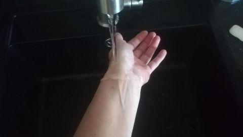 Ein Arm hält sich unter einem Wasserhahn, während frisches Wasser fließt – ein erfrischender Start in den Tag.
