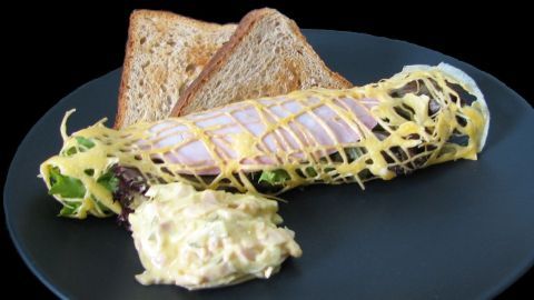 Ein gefülltes Spitzendeckchen auf einem schwarzen Teller, umgeben von zwei Toastscheiben und Salat, serviert mit Salatcreme.