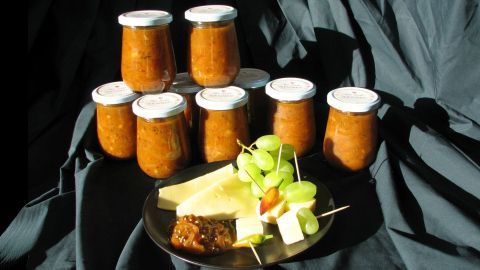 In der Mitte eines dunklen Tuchs stehen mehrere Gläser mit Mirabellen-Chutney, während eine Platte mit Käse und Trauben daneben steht.