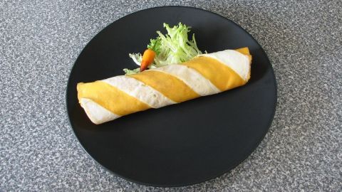 Ein gefülltes Zebra-Omelette liegt auf einem schwarzen Teller, eingerollt mit gelben und weißen Streifen, umgeben von einem kleinen Salat.