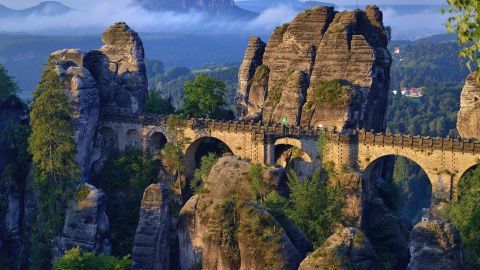 Eine beeindruckende Felsenbrücke überquert die zerklüfteten Sandsteingebirge der Sächsischen Schweiz, umgeben von Nebel.