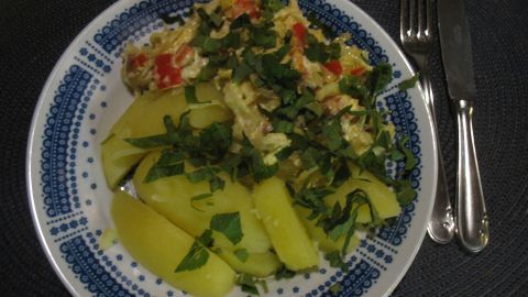 Auf einem Teller liegt Spitzkohl-Paprika-Rahmgemüse mit Katenschinken und Kartoffeln, umgeben von frischen Kräutern.