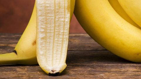 Eine aufgeschnittene Banane liegt neben mehreren ganzen Bananen auf einem Holztablett, illustriert die Nutzung von Bananenschalen bei Insektenstichen.