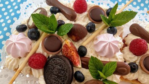 Ein einzigartiger Number Cake mit frischen Früchten und Schokolade liegt auf einem blauen, gepunkteten Tischtuch.