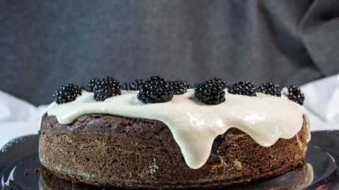 Ein Drip Cake mit einem saftigen Brownie-Boden, überzogen mit cremigem Frischkäse und garniert mit Brombeeren, steht auf einem silbernen Teller.