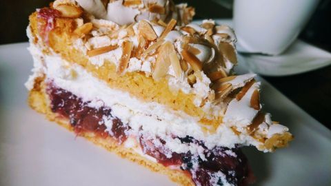 Eine luftige Himmelstorte mit Stachelbeeren und Sahnefüllung liegt auf einem Teller, umgeben von einem kleinen weißen Kaffeebecher.