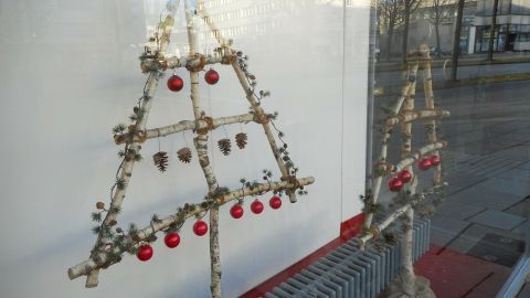 Ein dekorativer Christbaum aus Naturmaterialien steht vor einem Fenster, geschmückt mit roten Kugeln.