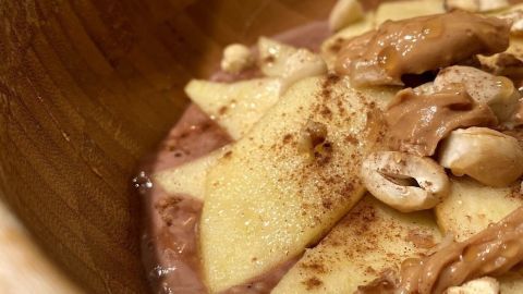Eine Holzschüssel mit kalorienarmen Pudding-Oats, garniert mit Apfelstücken, Nüssen und Zimt, sieht einladend aus.
