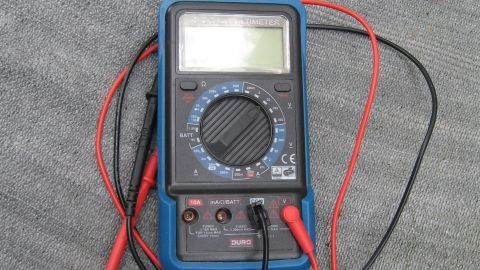Ein Multimeter liegt auf einem grauen Untergrund, während es mit elektrischen Testleitungen verbunden ist, um Messungen durchzuführen.