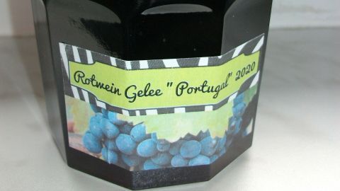 Ein Glas Rotweingelee steht auf einer hellen Oberfläche. Das Etikett zeigt bunte Trauben und den Schriftzug „Rotwein Gelee 'Portugal' 2020“.
