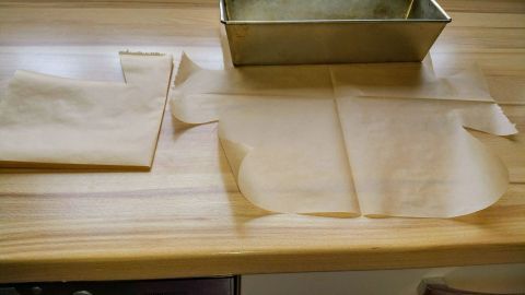 Auf einem Holztisch liegen zugeschnittene Backpapiere, während eine Backform Platz zum Füllen bietet.