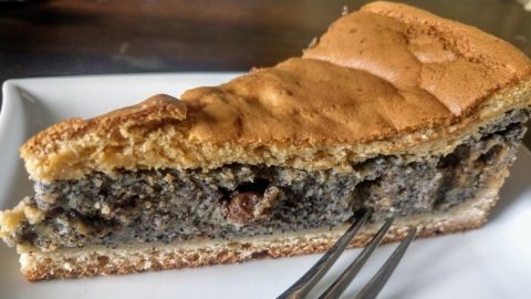 Ein Stück Thüringer Mohnkuchen liegt auf einem Teller, bereit zum Genießen, umgeben von einer dunklen Holzoberfläche.