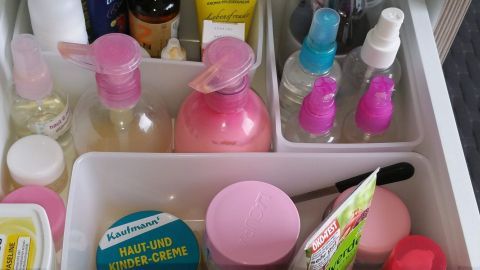 In einem Schublade sind mehrere Plastikdosen und Flaschen organisiert, die kosmetische Produkte enthalten.