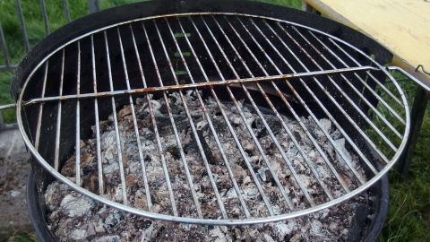 Ein Grillrost steht über glühender Kohle, bereit zum Reinigen mit Salatöl oder Zeitungspapier im Freien.
