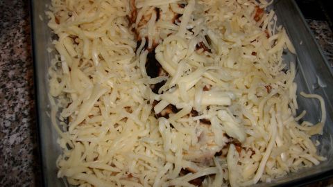 Ein Pfannkuchenauflauf mit Hack-Möhren-Füllung ist mit geriebenem Käse überbacken und steht in einer Backform auf einer Arbeitsplatte.