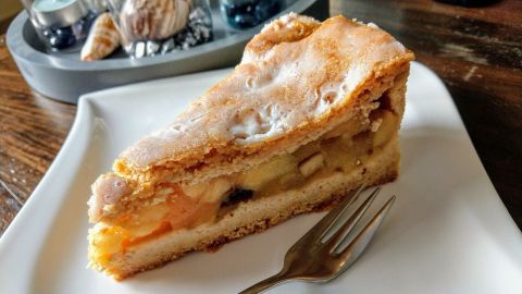 Ein Stück saftiger, gedeckter Apfelkuchen liegt auf einem weißen Teller, umgeben von einem stilvollen Tischsetting.