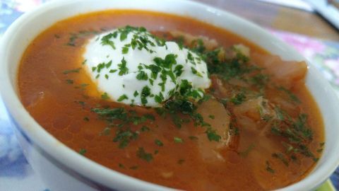 Eine Schüssel Borschtsch mit Sauerrahm und frischen Kräutern steht auf einem Tisch in einer gemütlichen Umgebung.