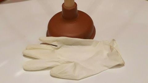 Ein Pümpel steht neben weißen Handschuhen auf einer hellen Oberfläche, bereit zur chemiefreien Abflussreinigung.