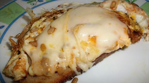 Zwiebelbrot mit Spiegelei wird überbacken mit geschmolzenem Havarti, serviert auf einem bunten Tellerrand.