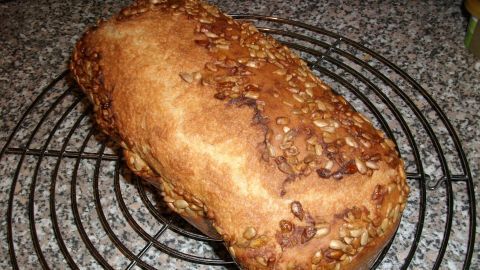 Braunes Dinkelbrot mit knusprigem Sonnenblumenkerne-Topping liegt auf einem Kuchengitter in einer Küchenumgebung.