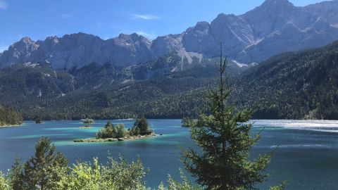 Der Eibsee glitzert unter strahlendem Himmel, umgeben von majestätischen Bergen der Zugspitze, die im Hintergrund aufragen.