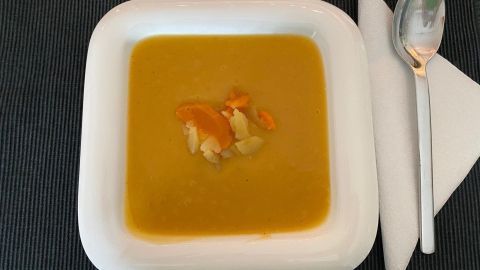 Eine cremige Kartoffel-Möhrencremesuppe in einer weißen Schüssel, garniert mit Gemüsestückchen, auf einem dunklen Tisch.