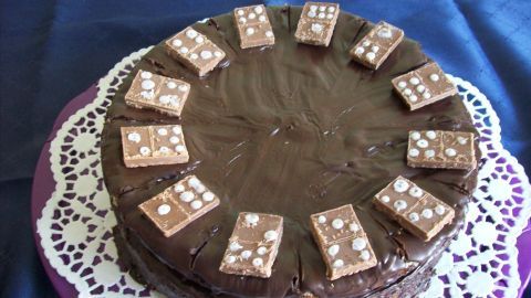 Eine rundliche Domino-Torte liegt auf einer filigranen Unterlage, dekoriert mit Schokoladenstücken. Sie strahlt köstliche Schokoladennoten aus.