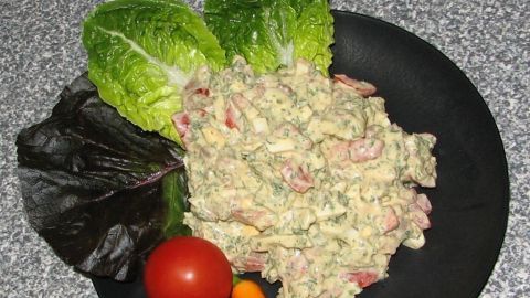 Ein dunkler Teller zeigt einen Schichtsalat mit einer cremigen Mischung aus gehacktem Gemüse, umgeben von frischen Salatblättern.