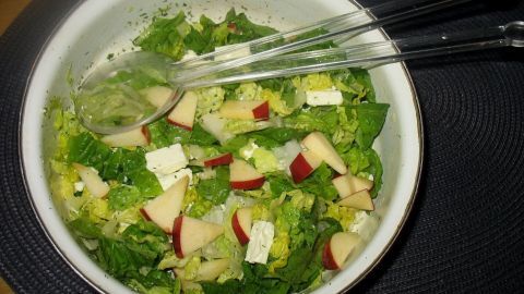 Ein Salat mit frischem Romana, Schafskäse und Äpfeln wird in einer Schüssel auf einem Tisch serviert.