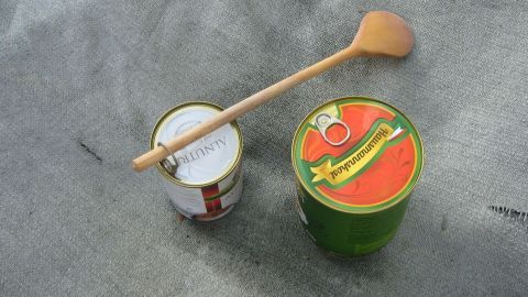 Eine Konservendose mit Ringverschluss steht auf einer grauen Oberfläche, während ein Holzlöffel darauf liegt, bereit zum Öffnen.