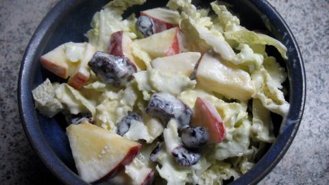 Ein frischer Chinakohl-Salat mit Apfel und Cranberrys liegt in einer Schüssel, umgeben von einer mottierten Oberfläche.