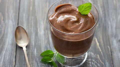 Ein cremiger Schoko-Minz-Pudding in einem Glas, garniert mit frischen Minzblättern, steht auf einer rustikalen Holzoberfläche.