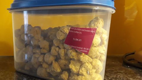 Ein durchsichtiger Vorratsbehälter steht auf einer Granitabdeckung. Er enthält gelbe Snacks und hat ein etikettiertes Haltbarkeitsdatum.