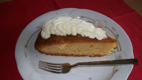 Ein Stück Beschwipster Orangenkuchen liegt auf einem Teller mit Sahnehaube, umgeben von rotem Tischdeck.
