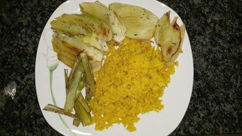 Fenchel liegt auf einem Teller, gebraten und schmackhaft, neben gelbem Reis und einigen Frühlingszwiebeln.