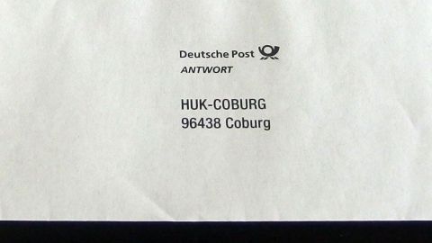 Eine Antwortkarte liegt auf einem weißen Umschlag, adressiert an HUK-Coburg in 96438 Coburg, für den Versand.
