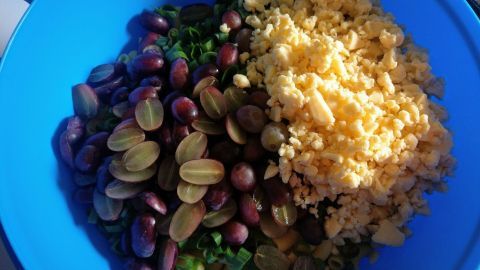 Ein bunter Nudelsalat wird in einer blauen Schüssel zubereitet, mit Nüssen und Trauben kombiniert.