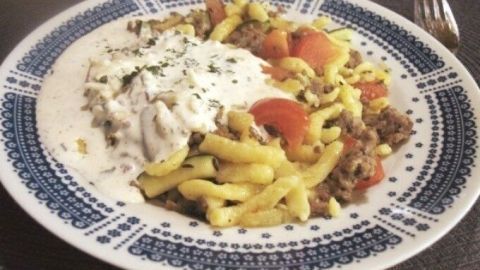 Eine dampfende Portion würzige Hack-Zucchini-Pfanne mit Spätzle und Kräuterschmand ist auf einem dekorativen Teller angerichtet.